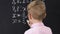 Little boy writing equation result on blackboard, school lessons, back view