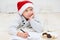 Little boy writing letter for Santa Claus. Child in red santa hat lying on bed  and thinking and writing christmas letter.