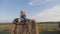 Little brother and older sister sitting on a haystack in a field at sunset and drink milk.