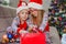 Little brother and sister in Santa hats on the sofa against the the Christmas tree take out decorations from the box