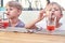 Little brothers drink juice with straws at wooden table