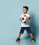 Little brunet boy in white t-shirt, denim shorts, khaki sneakers. Holding soccer ball, looking aside, posing on blue background