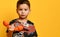 Little brunet child in camouflage t-shirt is holding a handset with wire, looking at you, posing against orange studio background