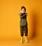 Little brunet child in khaki dino hoodie and pants, yellow rubber boots. He crossed his hands, posing on orange background