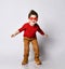 Little brunet model in sunglasses, red jumper, brown pants and sneakers. He smiling, spread hands, posing isolated on white