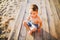 Little Caucasian boy child sitting on wooden pier sandy beach, summer time, sea vacation near water. The theme is the flow of time