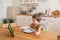 a little caucasian boy eats krunchy and watches tablet PC at kitchen table.