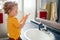 Little Caucasian boy toddler washing hands in bathroom at home. Health hygiene, morning routine for children. Cute funny child