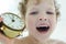 Little Caucasian curly boy yawns holding an antique clock.