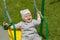 Little Caucasian girl 2 years old swinging on a swing and laughing cheerfully. Cheerful kid in a gray hat plays on the playground