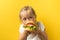 Little caucasian girl with blonde hair enjoying burger on a yellow background. Happy kid eating fast food burger