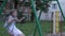 Little caucasian girl swinging on swing with chains at yard, looking at camera