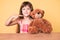 Little caucasian kid girl with long hair sitting on the table with teddy bear smiling happy pointing with hand and finger