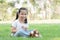 Little Caucasian kid girl smiling with dirty smeared lips milk. Cute child holding a glass of milk and sitting on green grass with