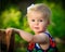 Little caucasian toddler stands using chair for support outside