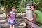 A little charming baby girl in a dress, with her young mother, drinking water from the spout of a Roman drinking fountain on a hot