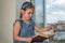 Little charming baby girl in a dress sitting on a windowsill near the window and reading a book