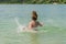 Little charming girl child bathes in a lake and plays splashing water