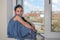 Little charming girl child in a dress, happy smiling, sitting on a windowsill near the window