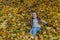 Little charming girl child throws up fallen yellow maple leaves in autumn park