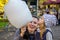 A little charming girl with her mama is eating huge cotton candy in an amusement park - a happy family