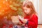 Little charming girl in pajamas helps her parents to decorate the Christmas tree early in the morning, examines the toy.