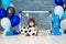 Little cheerful child dressed in sports clothes sitting on the floor near a football goal, looking at a big soccer ball. The first