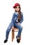 Little cheerful and very mobile girl in jeans suit and red cap posing sitting on a stool