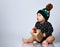 Little child in black bodysuit and hat with croco print, barefoot. He holding gift, sitting on floor isolated on white. Close up