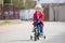 Little child, blond boy, learning how to ride a bicycle in the park using helping wheels on the side