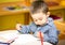 Little child boy drawing with colorful pencils in preschool at table in kindergarten