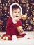 Little child boy dressed as santa playing with christmas decoration, dark background with illumination and boke lights, winter hol