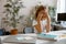 Little child closes eyes by hands sitting at table with supplies and laptop in room