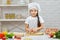 Little child girl in cap and an apron knead the dough
