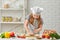 Little child girl in cap and an apron knead the dough