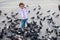 Little child girl feeding pigeons in the town square. Flock of rock doves crowding the street and eating discarded food.