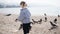 Little child girl feeds corn on the beach to pigeons.