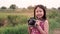 Little child girl holding medium format film camera and taking photo of sunset landscape with green field background