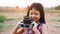 Little child girl holding medium format film camera and taking photo of sunset landscape with green field background