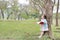 Little child girl reading book in summer park outdoor standing lean against tree trunk with looking to sky