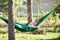 Little child girl relaxing in the green hammock and smiling at sunny summer day on holidays outdoor in the family garden.