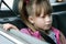 Little child girl sitting in a car on rear seat fastened with safety belt