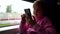 Little child girl is sitting at train and using smartphone with internet, playing game, touching screen