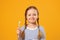 A little child girl in a striped pajamas holding a toothbrush. The concept of daily hygiene. Yellow background