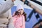 Little child girl in warm clothes, looking at camera, sitting on a banc on the railway station, waiting for urban train