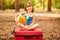 Little child girl wear swimsuit sitting on suitcase in summer forest with colorful ball. Vacation concept