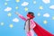 Little child plays superhero. Kid on the background of bright blue wall with white clouds and stars . Girl power concept