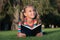 Little child reading book outdoors. Schoolgirl reading stories while relaxing green lawn. Cute pupil enjoy reading