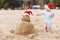 Little child in red santa hat with sand snowman on beach