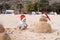 Little child in red santa hat with sand snowman on beach